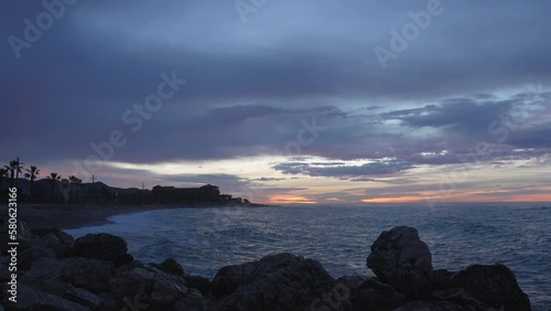 Nightfall beach bay man enjoys his time looking at sunset, sits on rocks photo