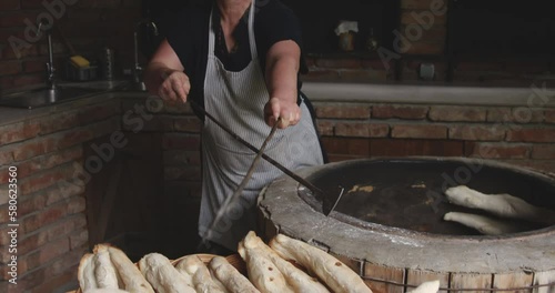 Woman Baker Removing The Baked Shoti Bread From A Rustic Round Clay Oven Using An Iron Stick.  Sighnaghi, Kakheti, Georgia - Slow Motion photo