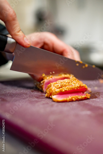 chef hands cut tuna into slices on a board in a restaurant kitchen
