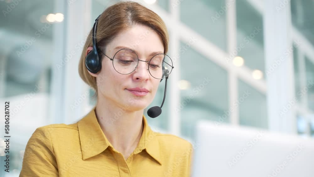 Close up face portrait of mature business woman support manager with wireless headset looking at the laptop screen and talking by online meeting conference video call help line at modern workplace 