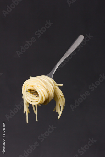 Fork with skein of spaghetti suspended on dark textured background.