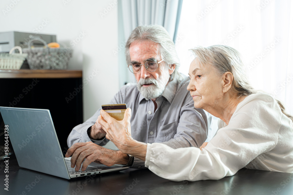 Cheerful mature retired couple shopping on Internet with ecommerce online app on laptop together at home,wireless communication.