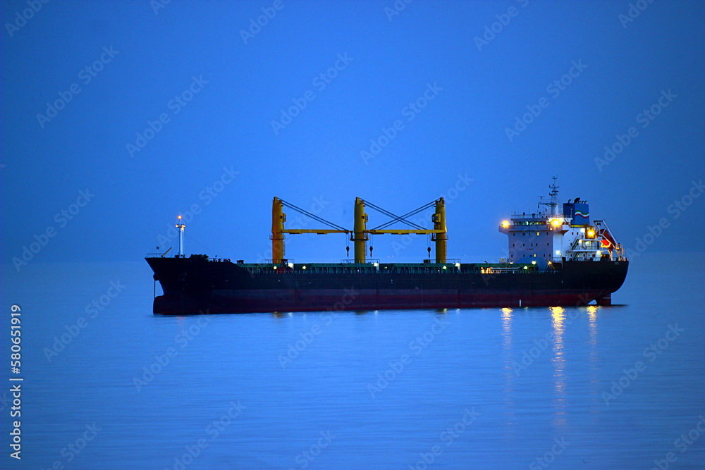 Glowing ship in the evening on the sea horizon with highlights on the water under the blue sky and in the blue water close-up