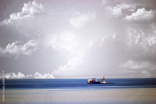 Tugboat, cranes and a ship on the sea horizon under a cloudy sky 