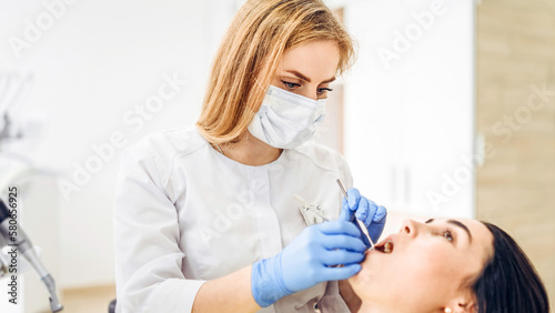 Female dentist with female patient in dental chair providing oral cavity treatment.