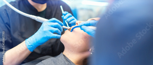 Female dentist and assistant with female patient in dental chair providing oral cavity treatment.