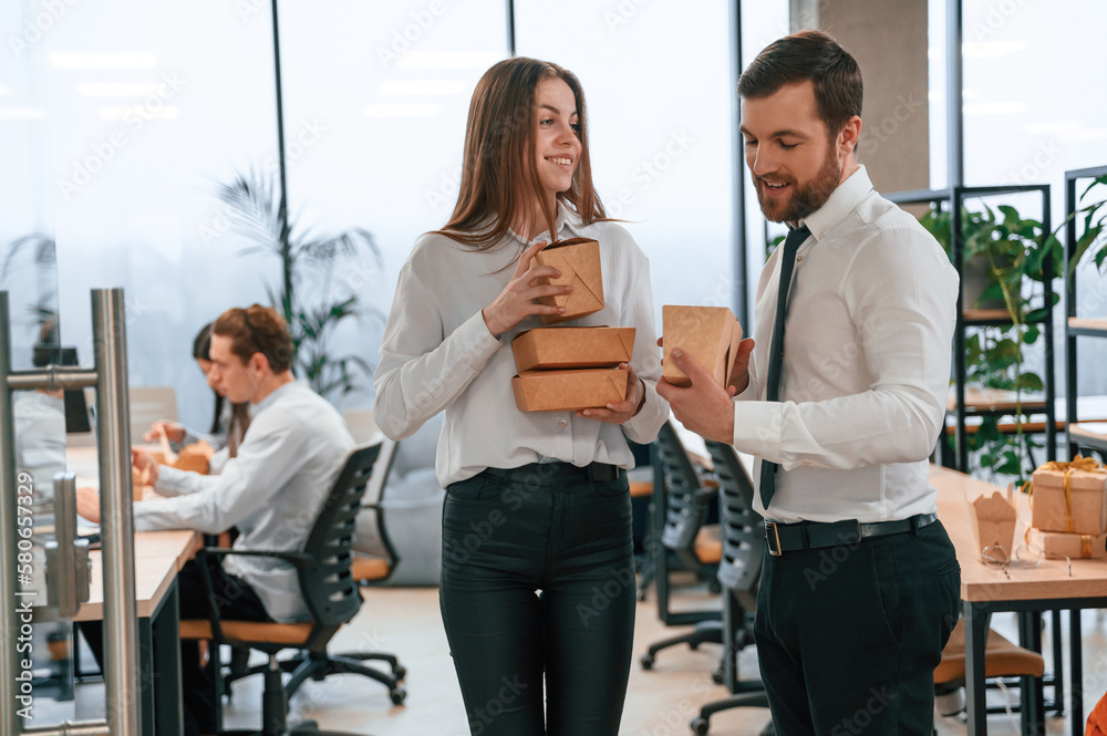 Front view. Man and woman are with eco boxes that is with food is in the office together Front view. Man and woman are with eco boxes that is with food is in the office together