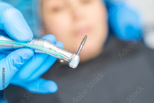 Closeup photo of dental implant in dentist hands with female patient in dental chair behind.