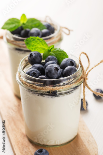 Two portion homemade Greek yogurt in a glass jars on white wood table. Healthy breakfast. Vertical orientation.