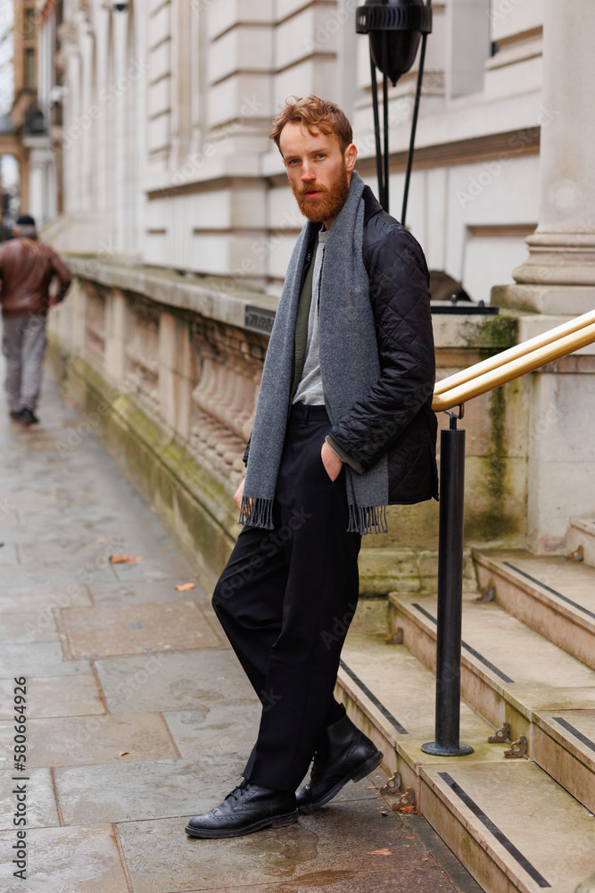 Bearded hipster leans against a railing in the middle of a London street