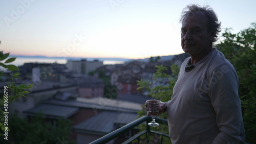 Mature man standing outside looking at scenic view while holding glass in sunset time. Retired senior older male person in 70s enjoying retirement