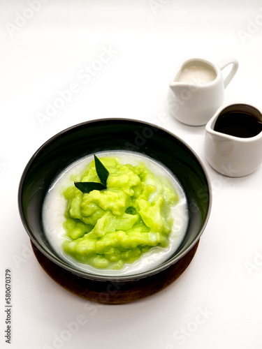 Bubur Sumsum Pandan is Indonesian rice flour porridge green colored by pandan leaves served with palm sugar sauce & coconut milk, garnish with pandan leaf in white bowl. On white background 