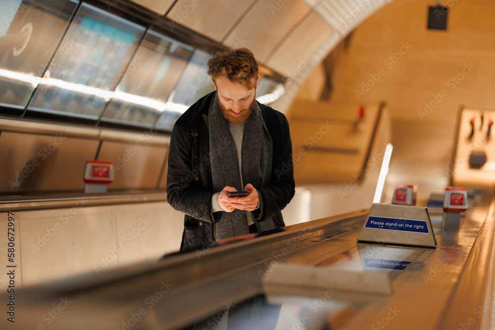 Fototapeta premium Bearded man using smartphone while standing on an escalator in the subway