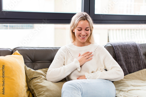 young pretty woman laughing out loud at some hilarious joke, feeling happy and cheerful, having fun sitting on a couch