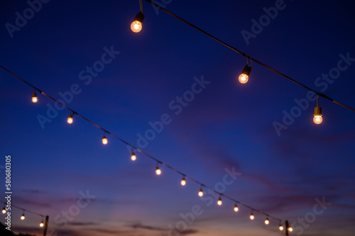 Festoon string lights decoration at the party event festival against sunset sky. light bulbs on string wire with copy space. Outdoor holiday background.