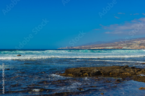 Wallpaper Mural Surfing in the stormy ocean on a pebble beach. Foamy waves on a sunny day. Rocky coastline with surf in the Atlantic Ocean. Playa Honda las Americas beach, Tenerife, Spain, Desember 2019. Torontodigital.ca