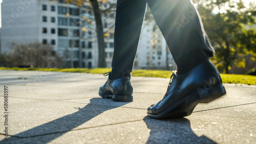 Legs of a businessman in fashionable shoes walking outdoors. Business concept. Close-up view to the businessman in a black new shoes walks on the street. Stylish men wears. Low angle. Rear view. © Valua Vitaly