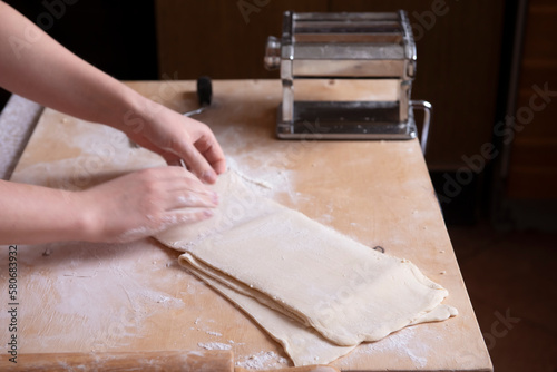 Close-up of the process of cooking homemade pasta. The chef prepares fresh traditional Italian pasta. Top view of the hands of a girl who is folding dough for further work. italian cuisine at home