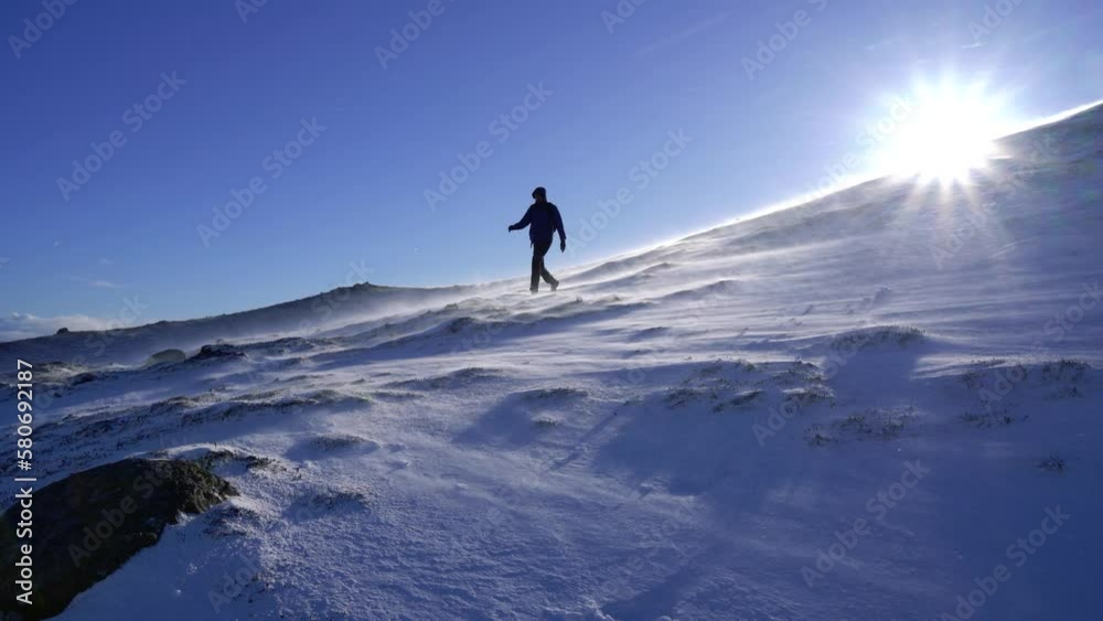 Hiker walking between blowing snow on a mountain side in winter time in Scotlad. Steady shot Hiker walking between blowing snow on a mountain side in winter time in Scotlad. Steady shot