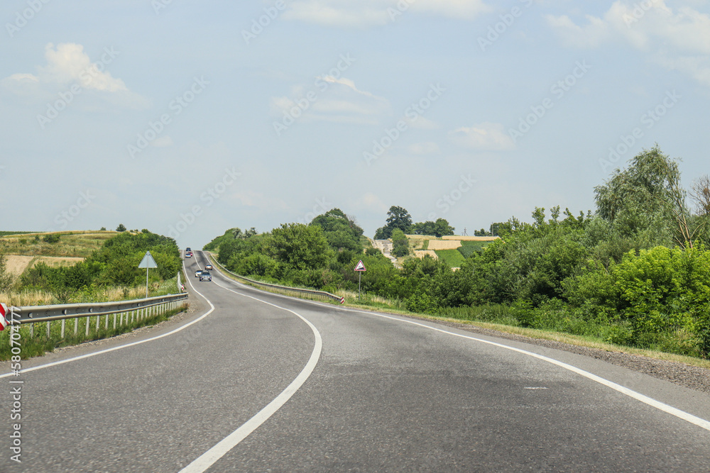 A winding two-lane road against the backdrop of picturesque landscape. Greenery by the road. Summer, travel, cars. Photo, country landscape, Ukraine