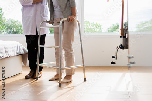 Caucasian male doctor helping female patient try to walk with walker. Doctor is examining the patient in the hospital.