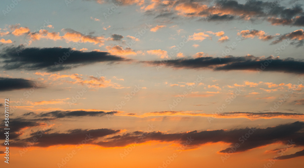 Fototapeta premium An unbelievably beautiful summer sunset. Yellow-orange clouds against a barely blue sky. The sun's rays from below illuminate the clouds. The beauty of nature. A summer sunset.