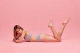 Young thin girl with short brown hair wearing grey underwear lying on floor over pink color background. Concept of natural beauty, body and skin care, healthy eating