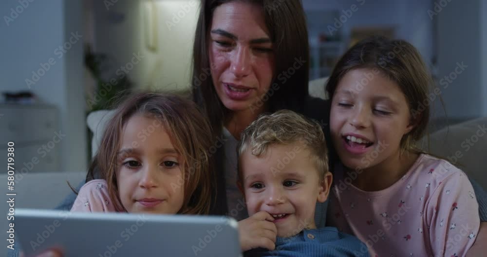 Small Family Using Digital Tablet to Have a Video Call with Distant Relatives While Sitting at Home With Pyjamas. Happy Young Mother and her Children Talking to Friends Using the Internet