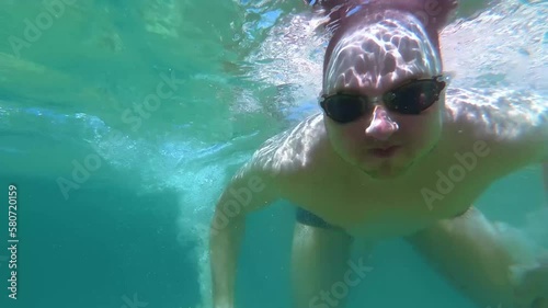 Young man is swimming underwater closeup and crossing his arms in the form of heart. 2,7K