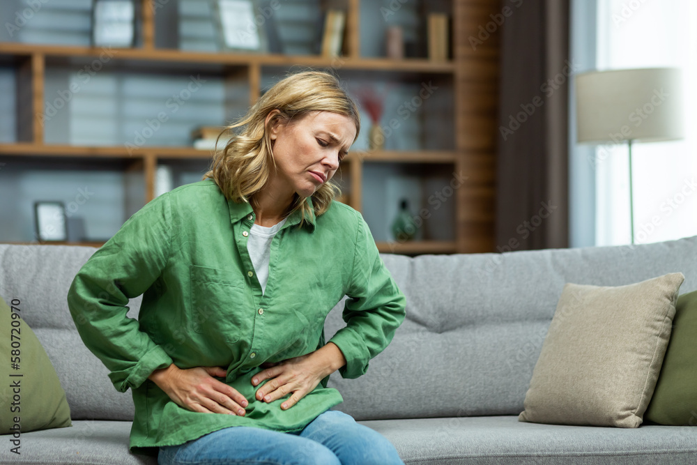 Unhealthy senior woman sitting on sofa at home. holding her stomach