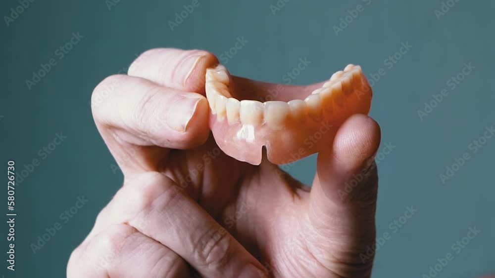 Hand Elderly Holding a Removable Upper Jaw Denture on a Blurred