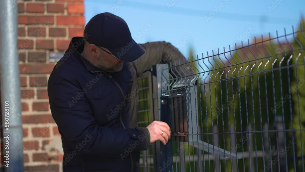 Working home installing post mailbox on metal fence outdoor. Man in casual clothes working in house yard, handmade work concept Working home installing post mailbox on metal fence outdoor. Man in casual clothes working in house yard, handmade work concept