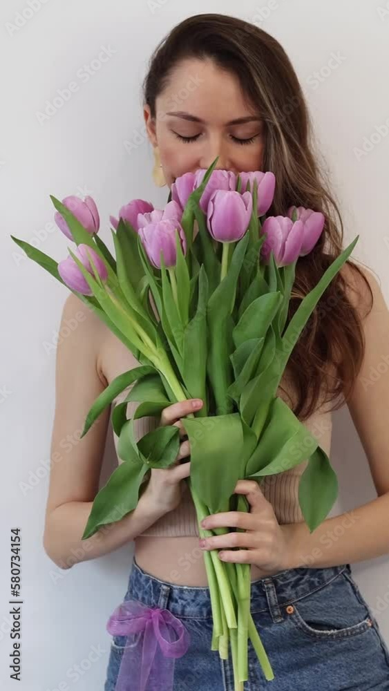 Beautiful young woman with a bouquet of pink tulip flowers on a white background. The girl shows flowers to the camera. Vertical Video. Beautiful young woman with a bouquet of pink tulip flowers on a white background. The girl shows flowers to the camera. Vertical Video.