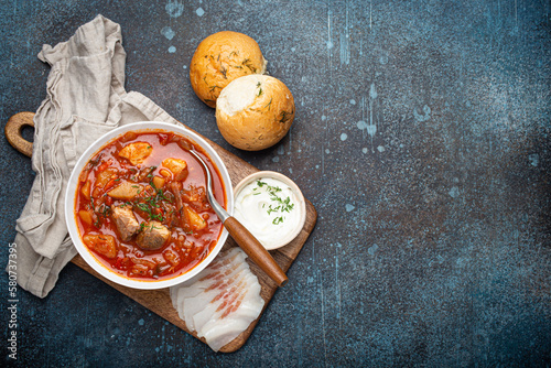 Ukrainian Borscht, red beetroot soup with meat, in white bowl with sour cream, garlic buns Pampushka and salo slices on rustic stone background. Traditional authentic dish of Ukraine, space for text