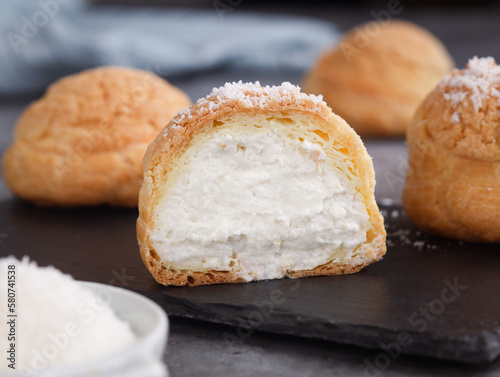 A French cream puff crack bun (Choux au Craquelin) in a plate, cut in a half filled with cream coconut filling topped with coconut grated. It's a dessert base of savory choux dough bun 