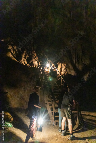 Local tour guide with traditional lantern guiding tourists through the dark chambers of Tham Nam Lod caves © ThamKC