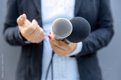 Female journalist holding microphone and gesturing during media interview. Freedom of the press concept.