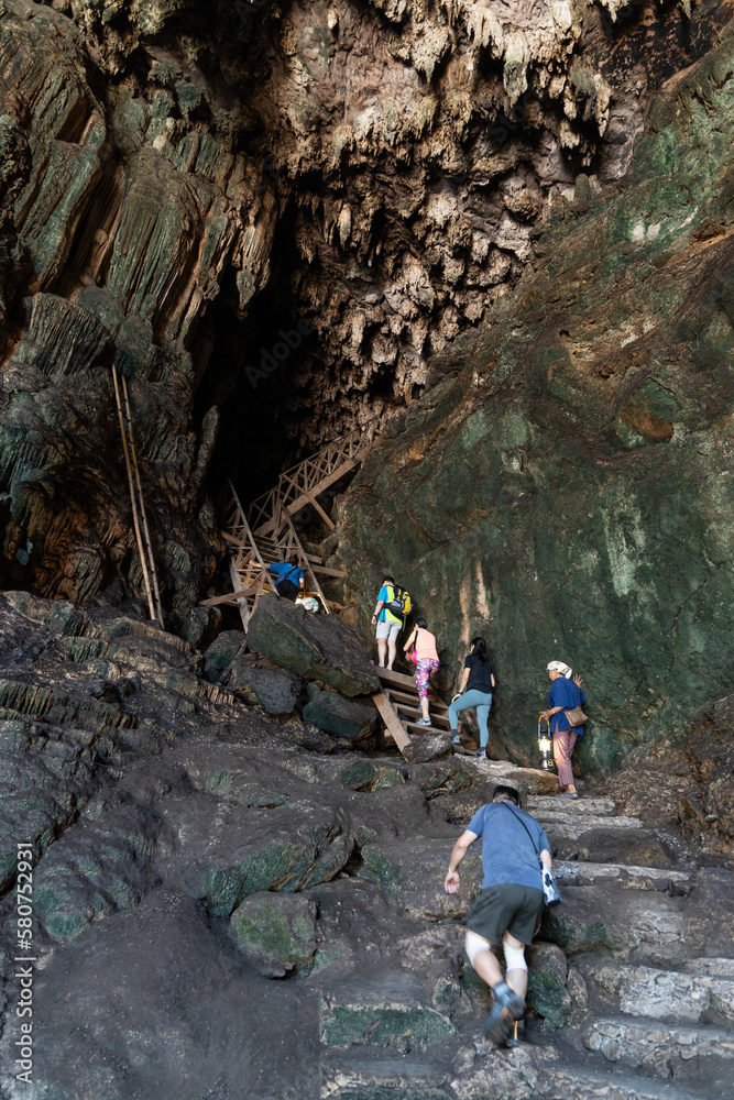 Fototapeta premium Local tour guide with traditional lantern guiding tourists through the tall and dark chambers of Tham Nam Lod caves