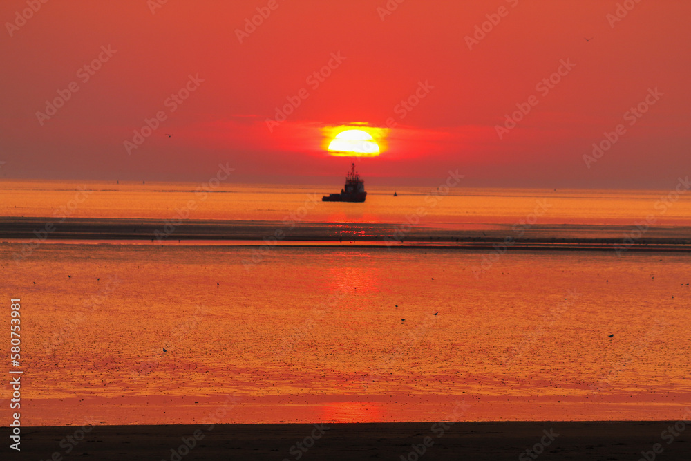 A stunning sunset at the beach. A boat approaches the falling sun as a couple look on from the sand. A stunning sunset at the beach. A boat approaches the falling sun as a couple look on from the sand.