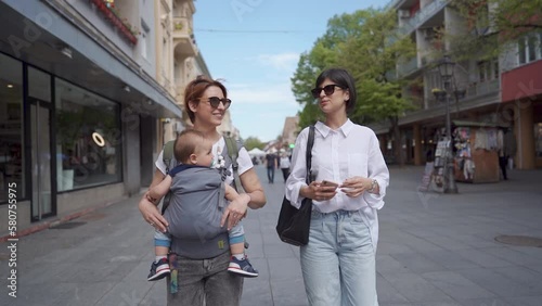 Two young women are walking in the city street with baby. The concept of family and healthy lifestyle. Mother whit baby