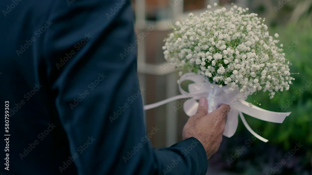 A groom walks with a bouquet of white flowers to the bride on their wedding day. A groom walks with a bouquet of white flowers to the bride on their wedding day.