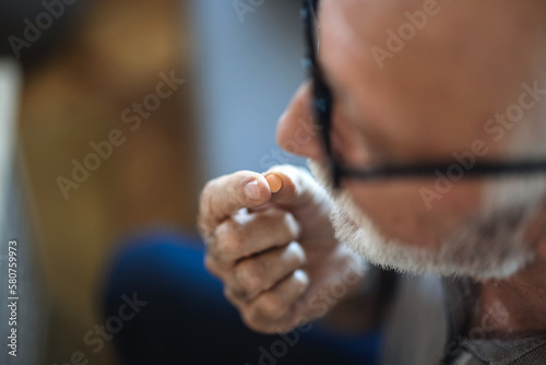 Close up of old man taking a pill at home. Old man taking a pill. Cropped shot of a senior man sitting alone in his living room and taking pills.