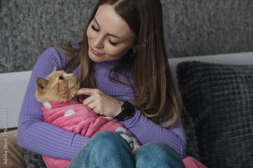 A young woman in her bedroom holds her pet cat wrapped in a baby blanket in her arms. Love and care for animals, childless woman. Treating animals like your children A young woman in her bedroom holds her pet cat wrapped in a baby blanket in her arms. Love and care for animals, childless woman. Treating animals like your children