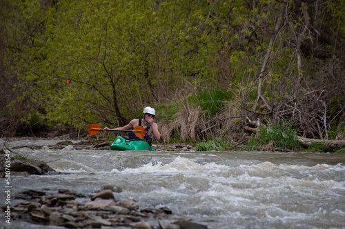 A man in a white water kayak drinks from the river with his hand