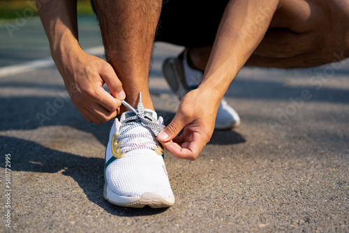 sporty handsome Asian man tying shoe laces getting ready for jogging in city public park on summer day, young guy workout running outdoor for healthy and active lifestyle