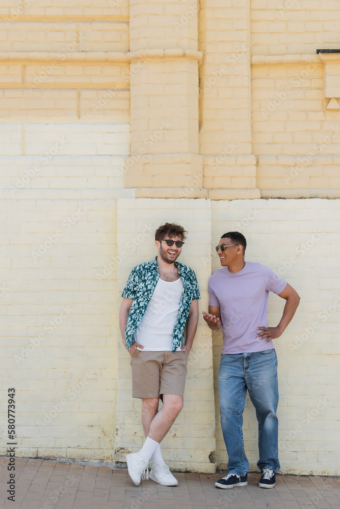 Smiling african american man talking to friend in sunglasses near building on street in Kyiv.