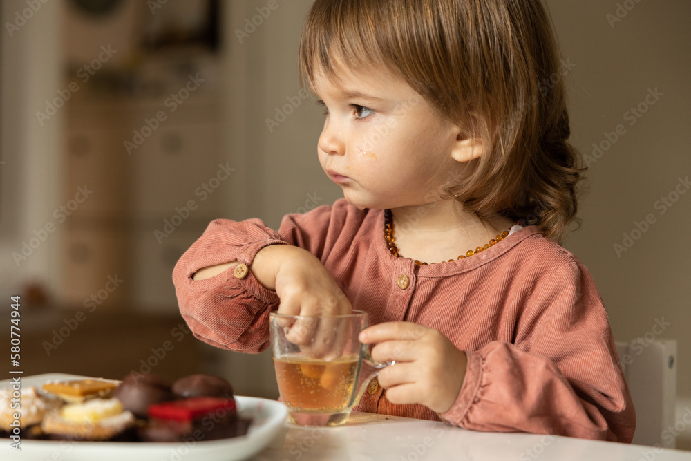 Little girl eats at the table and sticks her fingers into a glass of drink. Little girl eats at the table and sticks her fingers into a glass of drink.