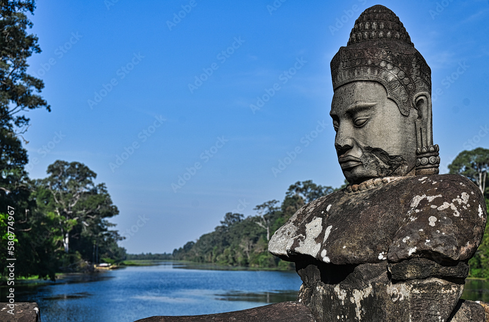 Fototapeta premium Carving of a Monk Sitting Above View of River Lined with Trees in Cambodia