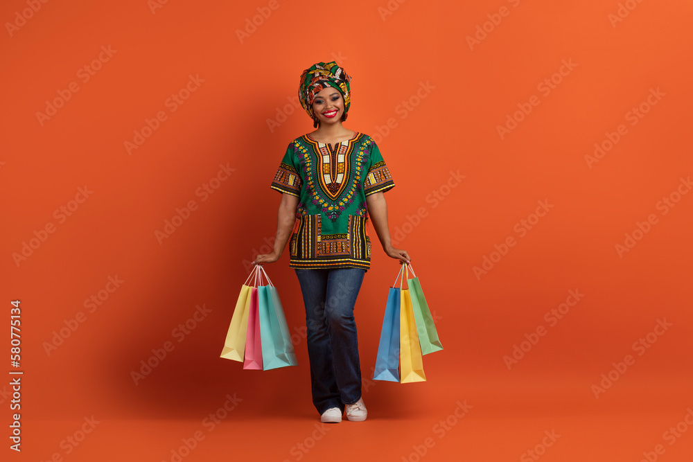 Happy black lady in african costume posing with her purchases