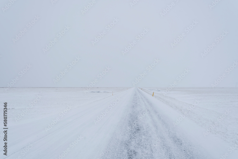 Straight icy road on a remote location in Iceland during winter with almost no difference between the snowy land and sky. Straight icy road on a remote location in Iceland during winter with almost no difference between the snowy land and sky.